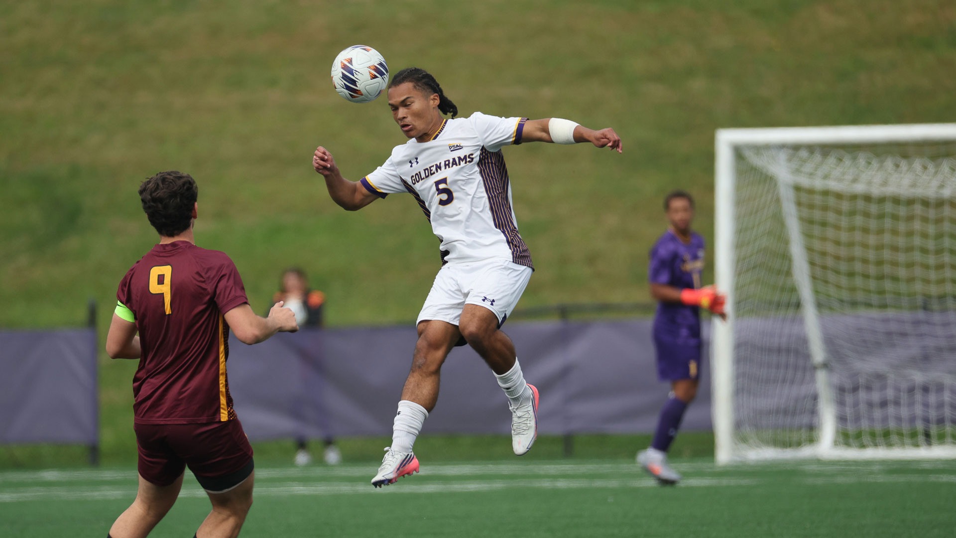 Kenyon Carter wearing white uniform with purple number and text elevates for a header against Gannon in front of gannon player number 9 wearing maroon jersey and gold number