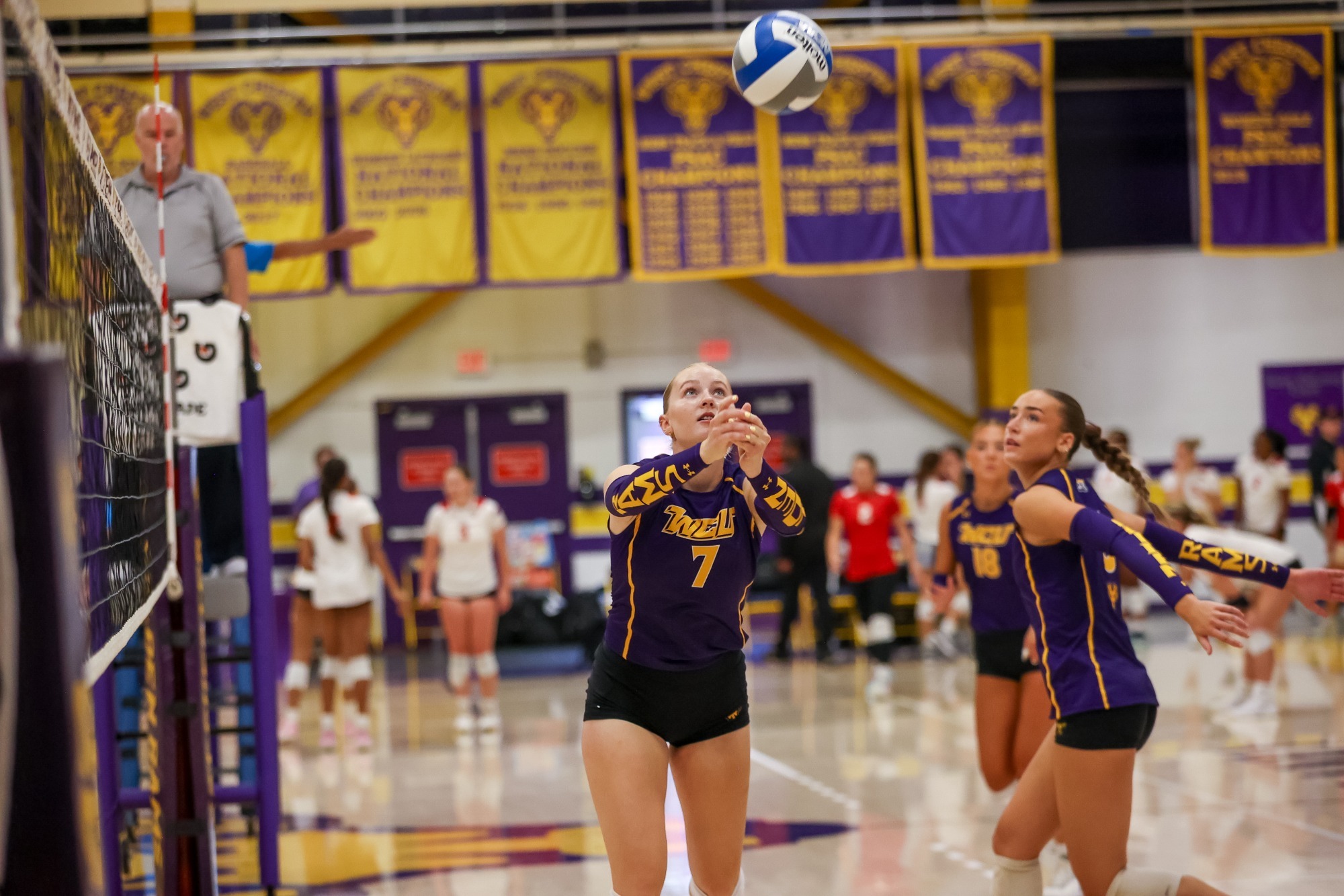 Bria Stepp wearing purple and gold sleeveless top with Golden Rams armsleeves looking to set vs WVSU as Brooke Forester prepares to jump for an attack
