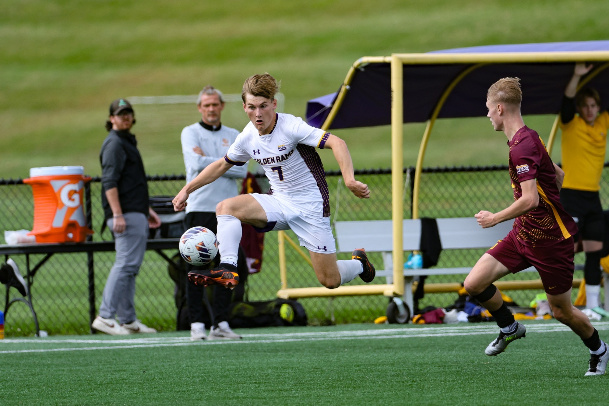 Joshua Rick wearing home white kit with black and orange cleats elevates in front of a gannon defender wearing all maroon and plays a cross off his left foot across the box to cannon dalton for an assist on Dalton's first collegiate goal on Saturday vs Gannon