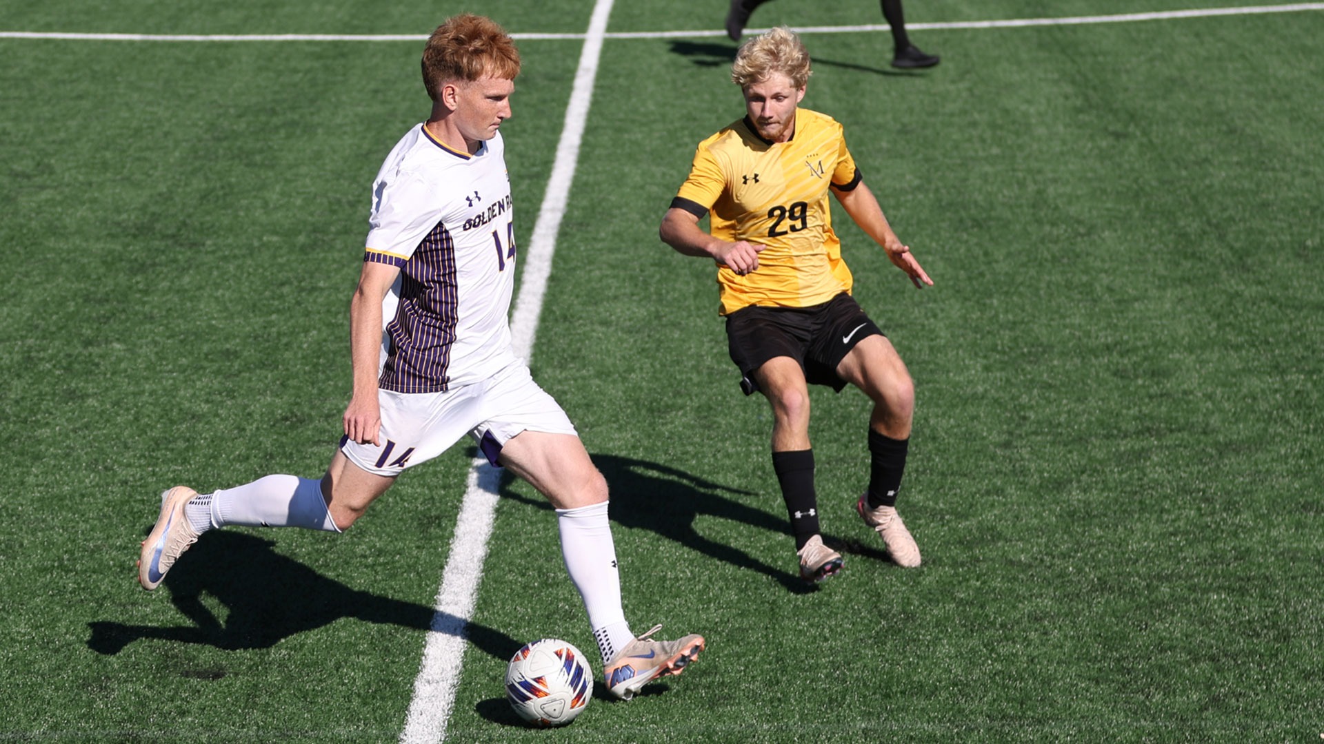 Peter Tichy wearing home white on white kit looks for space up the sideline vs a Millersville defender wearing gold top and black shorts on Rockwell Field on Wednesday
