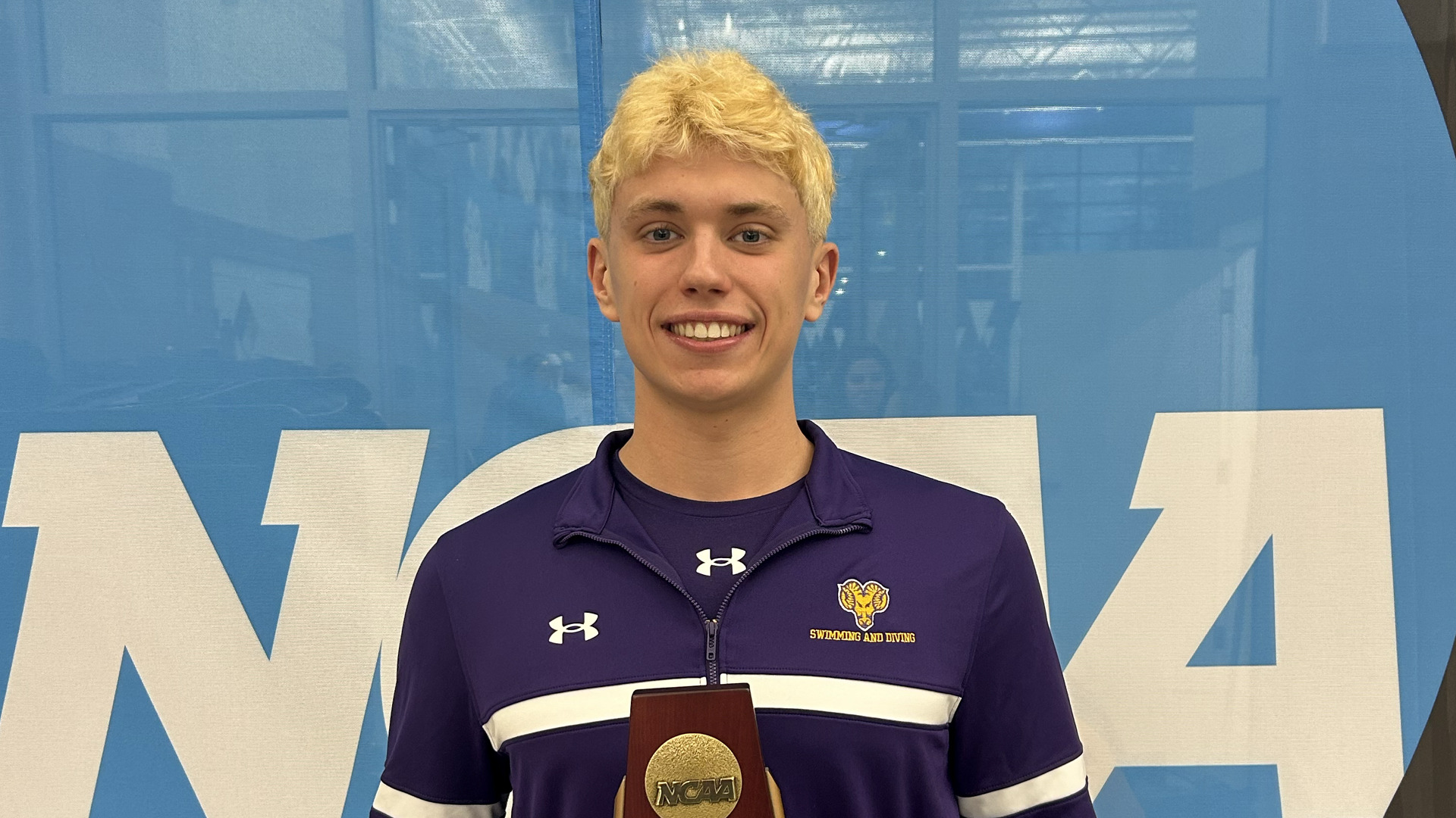 Paul Demesy poses in front of the NCAA logo with his fourth-place mini trophy in the 1000 freestyle