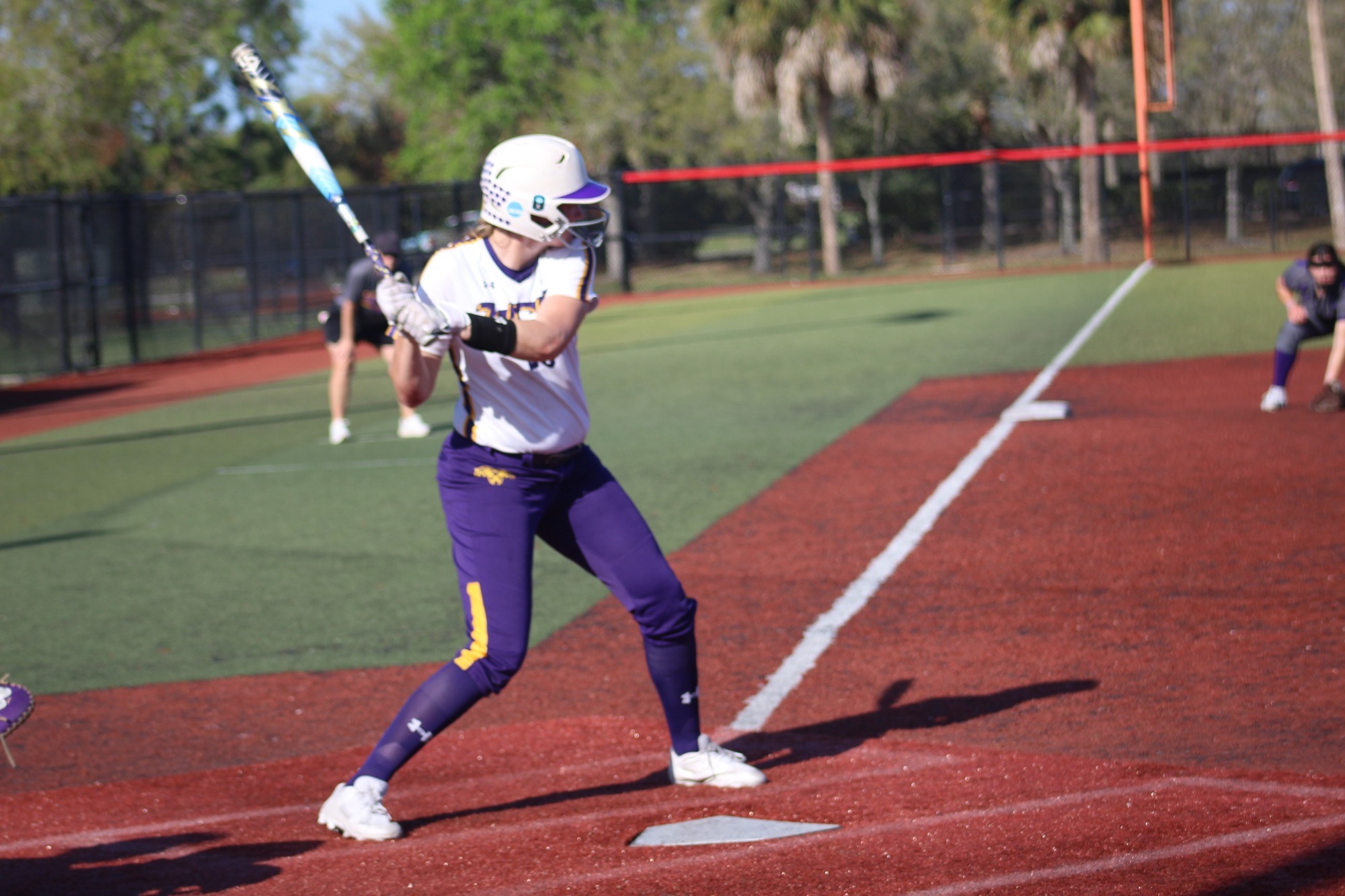 Mairead Hopkins begins to swing wearing white and purple game uniform at Space Coast Games in Melbourne, Florida