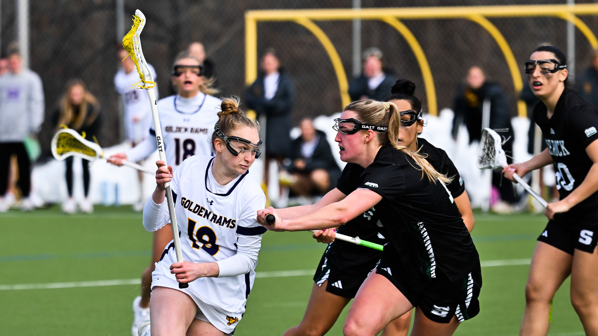 Kendall Fortune leans into a Slippery Rock defender while dodging to the goal in her home white jersey with purple trim and purple letters and numbers.