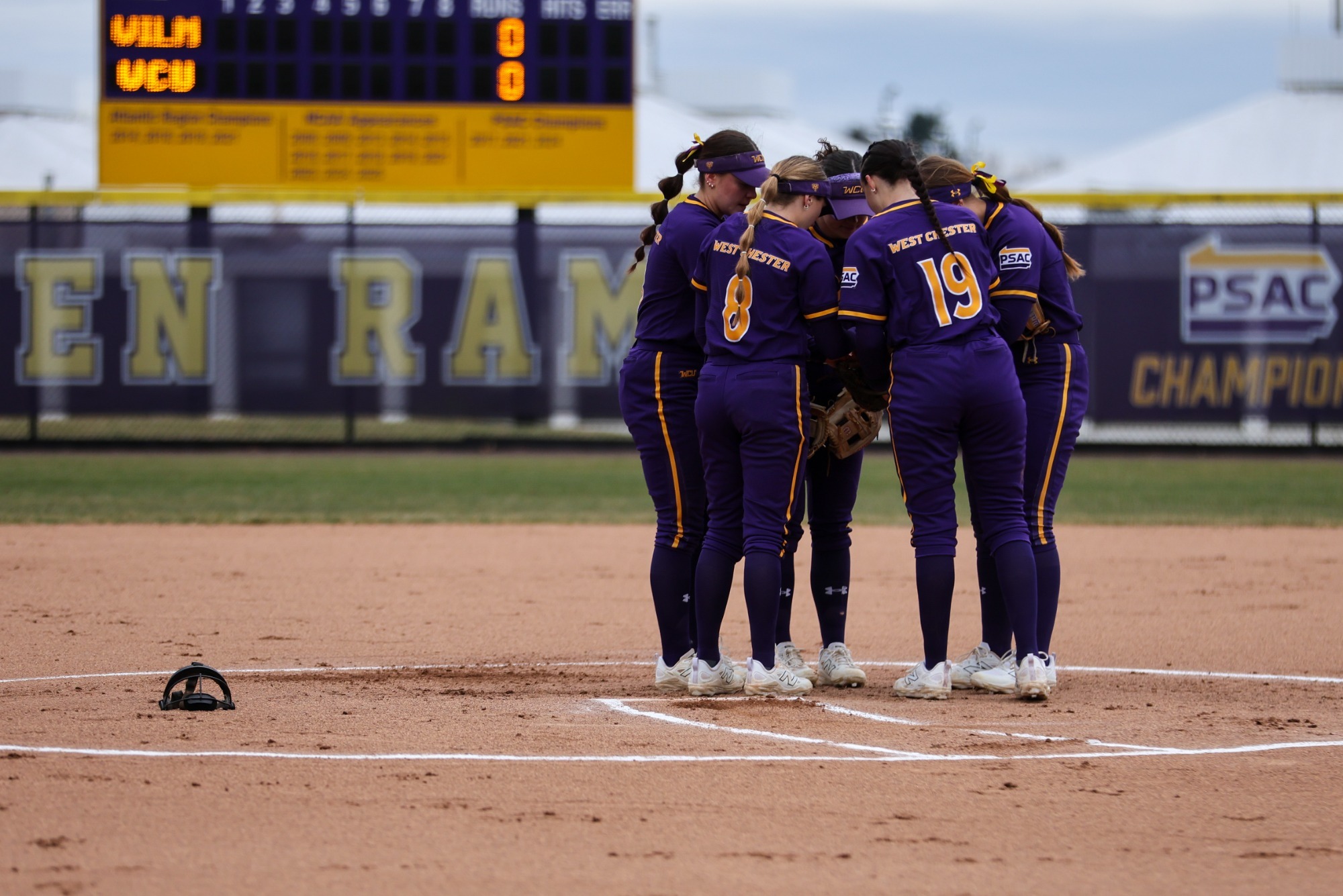 SOFTBALL TEAM IN NEW HOME PURPLE UNIFORMS IN HUDDLE BEFORE WILMINGTON DOUBLEHEADER