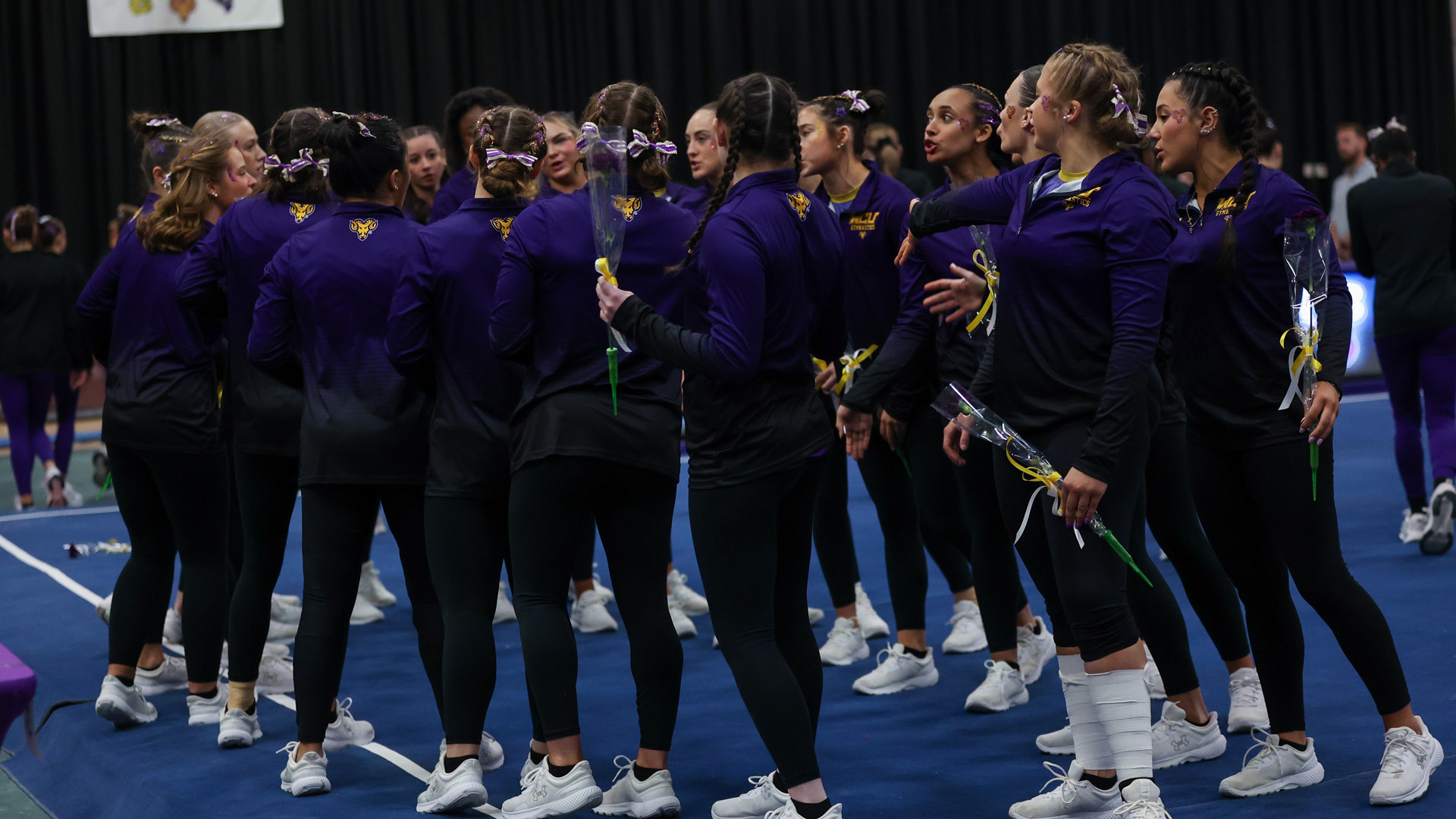 WCU Gymnasts Gather on the Floor Exercise apparatus in their purple warm ups holding one single yellow rose before the team finals of the WCGNIC Championships inside Hollinger Fieldhouse