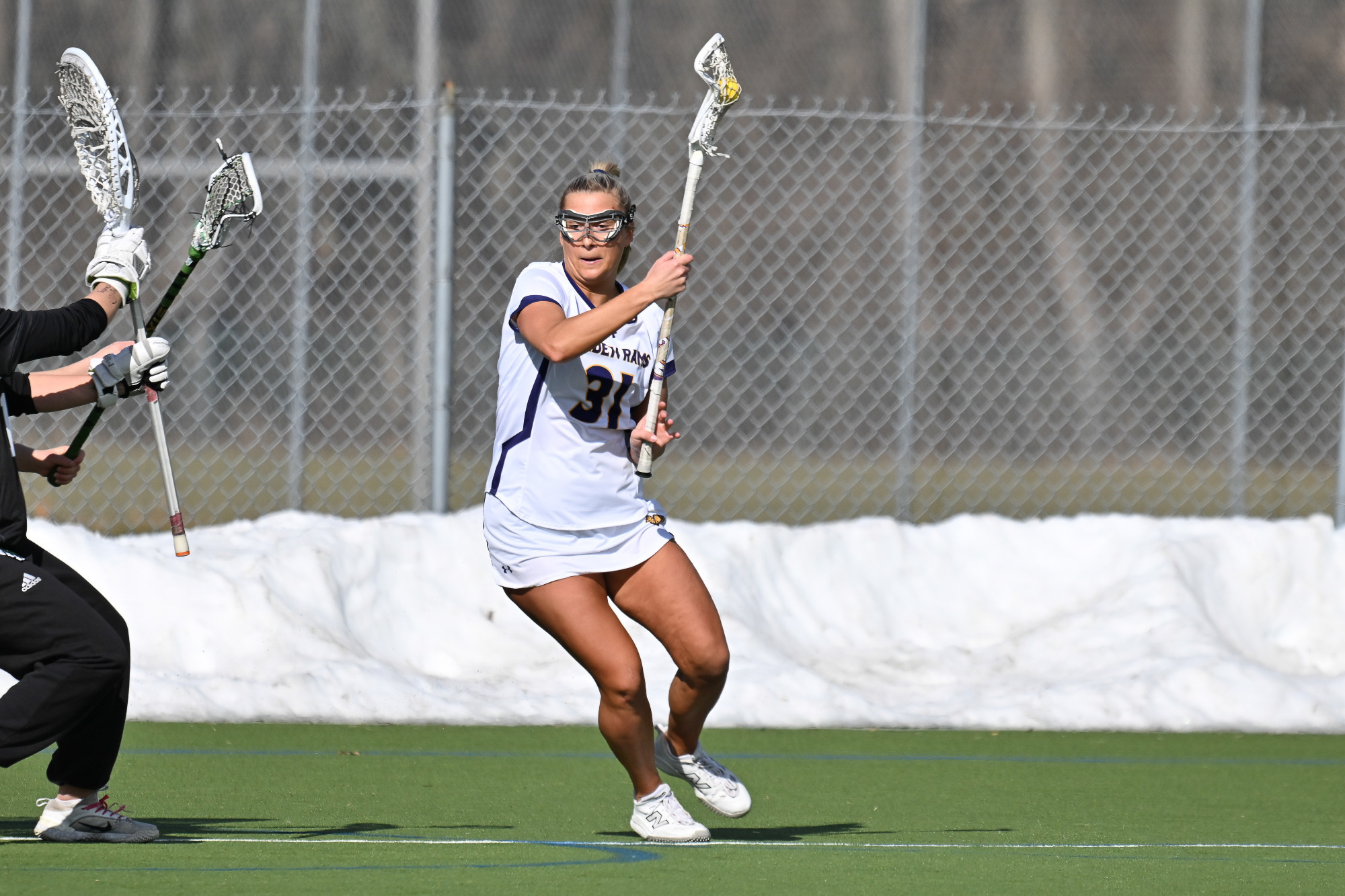 Sydney Wasdick, wearing WCU's home white jerseys with purple trim and white sneakers, roll dodges from behind the cage around the right side during the Slippery Rock game in February at Vonnie Gros Field..