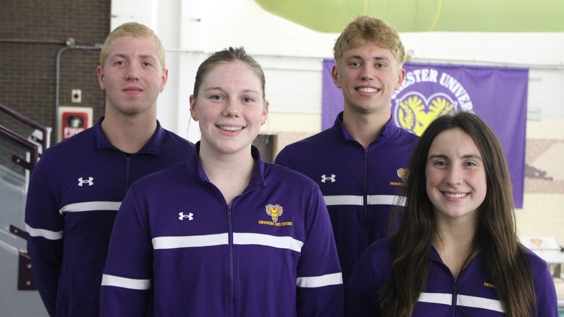 WCU Swimming National Qualifiers pose for a photo on the deck of the pool in their purple warm up jackets from left to right: Marti Rosell Diez, Greta Saville, Paul Demesy and Lenya Ryan.