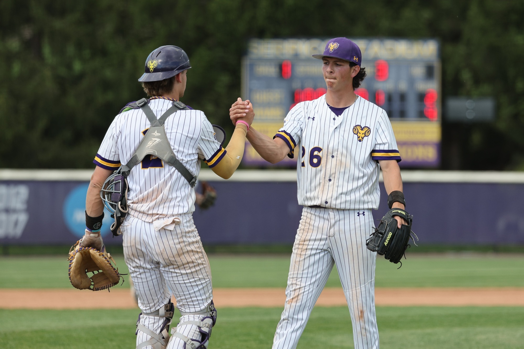 Landen Rozich and Caleb Strawhecker wearing white pinstripe uniforms with dirt stains shake hands in front of the mound following win over Shepherd on 4/17