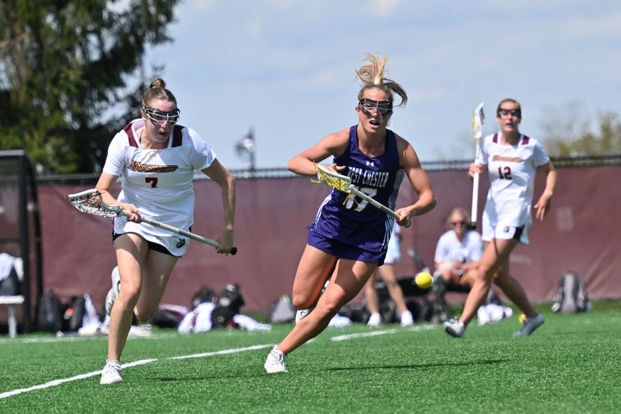 Riley MacHenry chases a defender down at Bloomsburg in her purple road jersey with white numbers and letters and white trim.