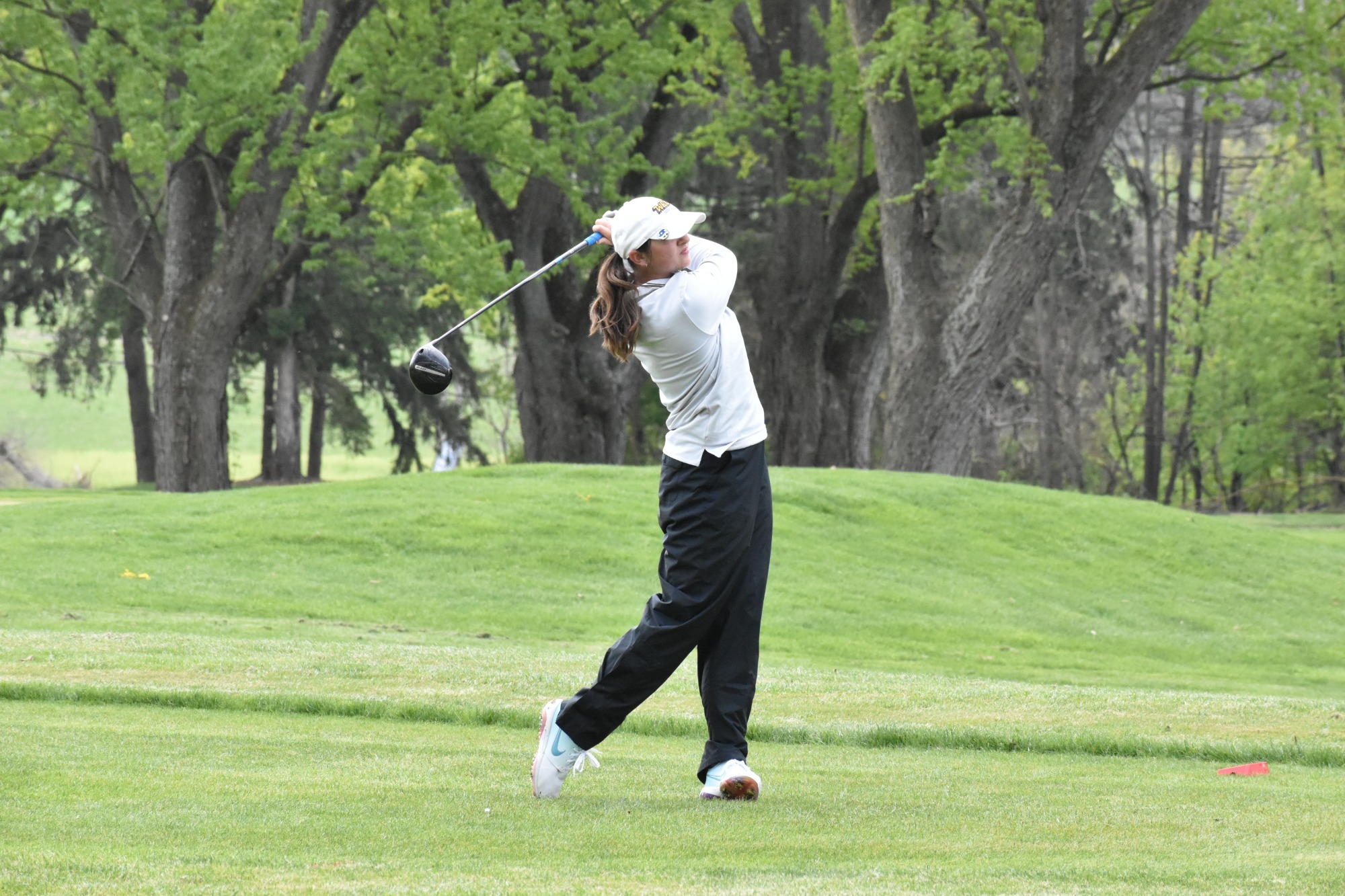 Cara Murphy at the PSAC Women's Golf Championships wearing white pullover and black rainpants finishing her opening tee shot on the first hole