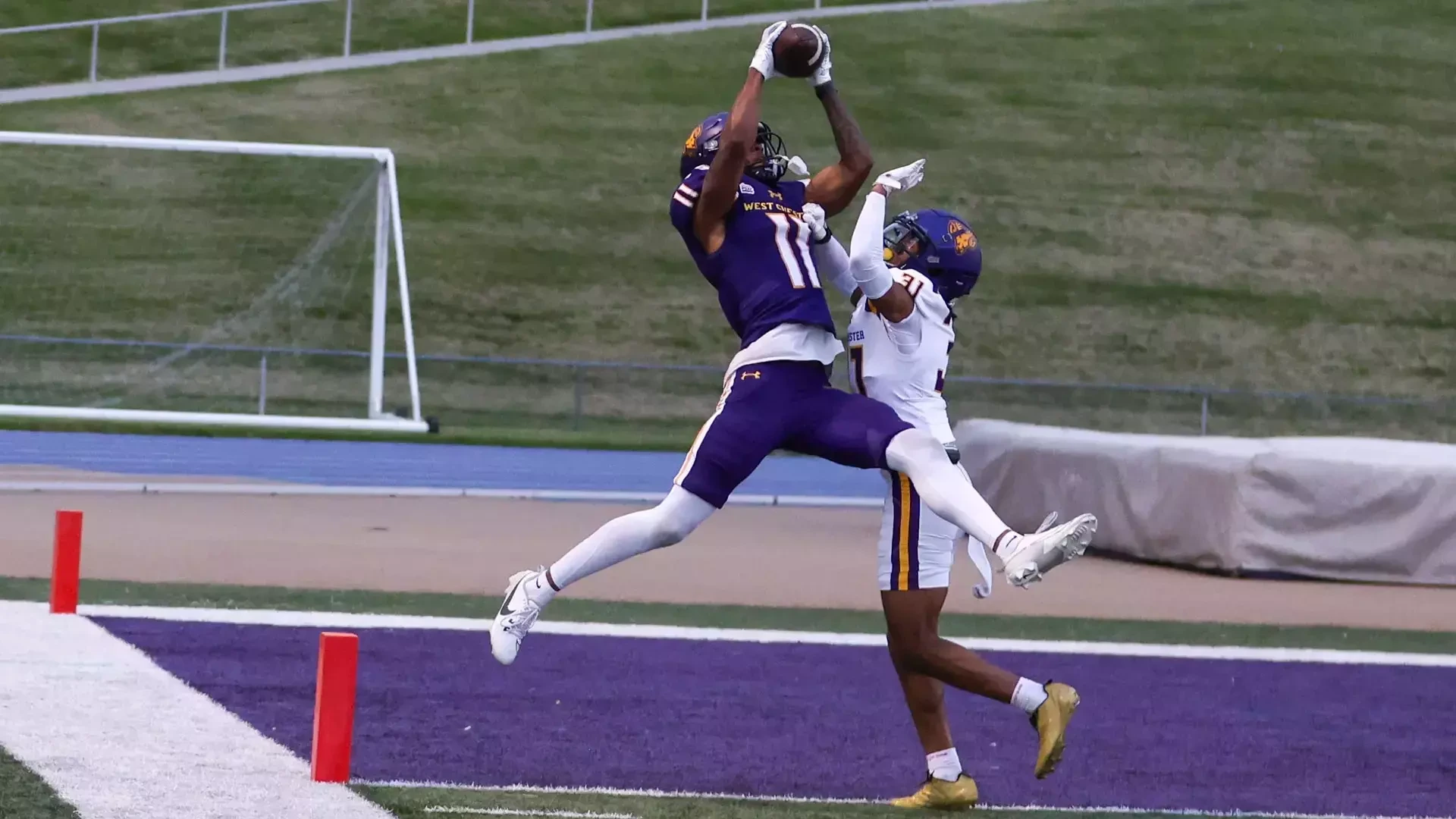 Blake Thomas makes a leaping catch in the front corner of the end zone over Pedro Reyes during the Purple-Gold Intersquad srimmage. Thomas is wearing the Golden Rams' purple uniformns with white numbers in gold trim while Reyes is wearing the team's road white jerseys with purple numbers and purple-gold stripes around the top of the shoulder