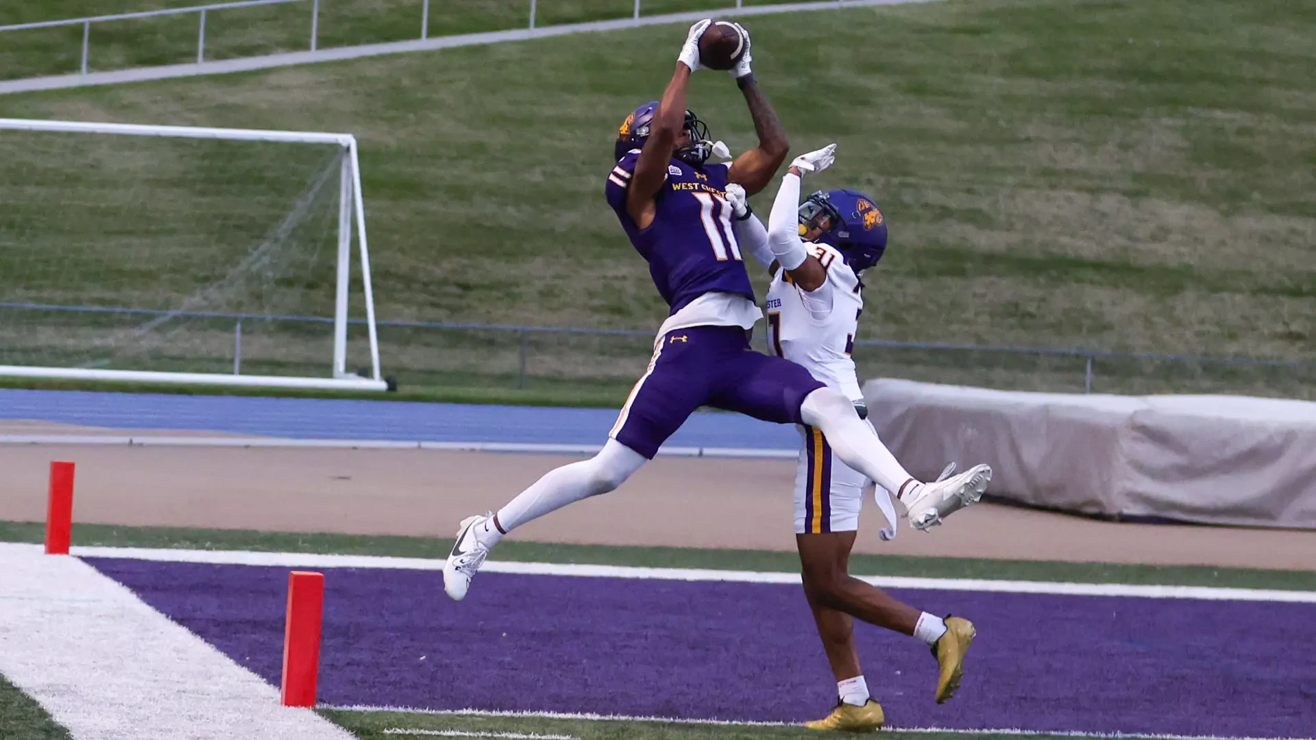 Blake Thomas makes a leaping catch in the front corner of the end zone over Pedro Reyes during the Purple-Gold Intersquad srimmage. Thomas is wearing the Golden Rams' purple uniformns with white numbers in gold trim while Reyes is wearing the team's road white jerseys with purple numbers and purple-gold stripes around the top of the shoulder