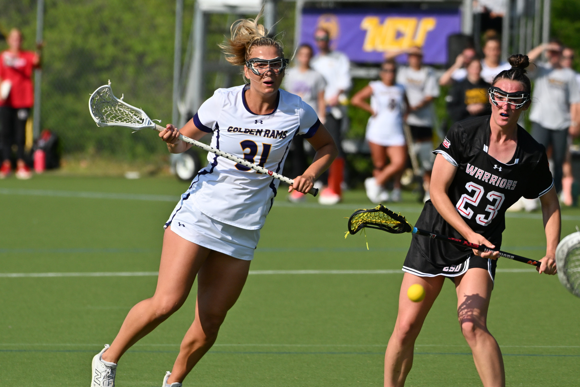 Sydney Wasdick battles for a loose ball against ESU in her home white jersey with purple numbers in gold trim while ESU is wearing their road black jerseys with white numbers and a red stripe going through the middle