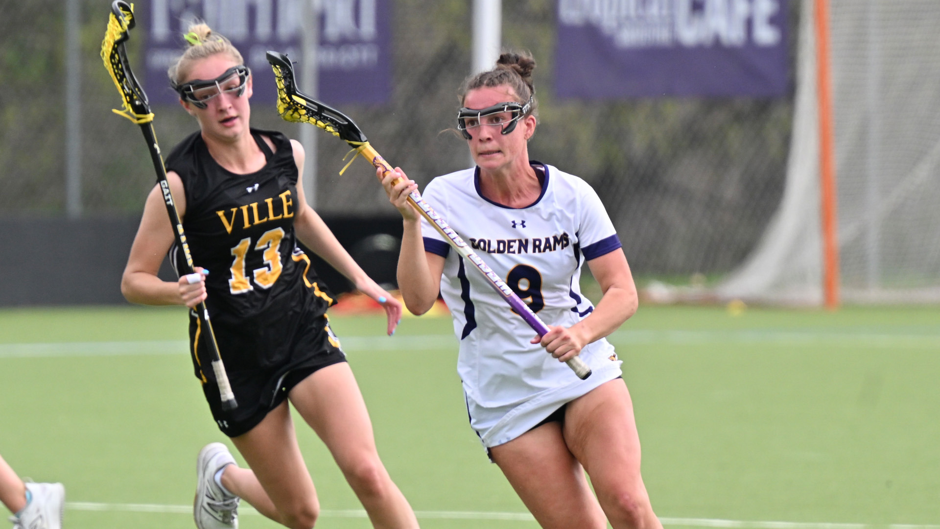 Caitlin Trickett races up field past a Millersville defender at Vonnie Gros Field in her home white jersey with purple numbers and letters and gold trim.