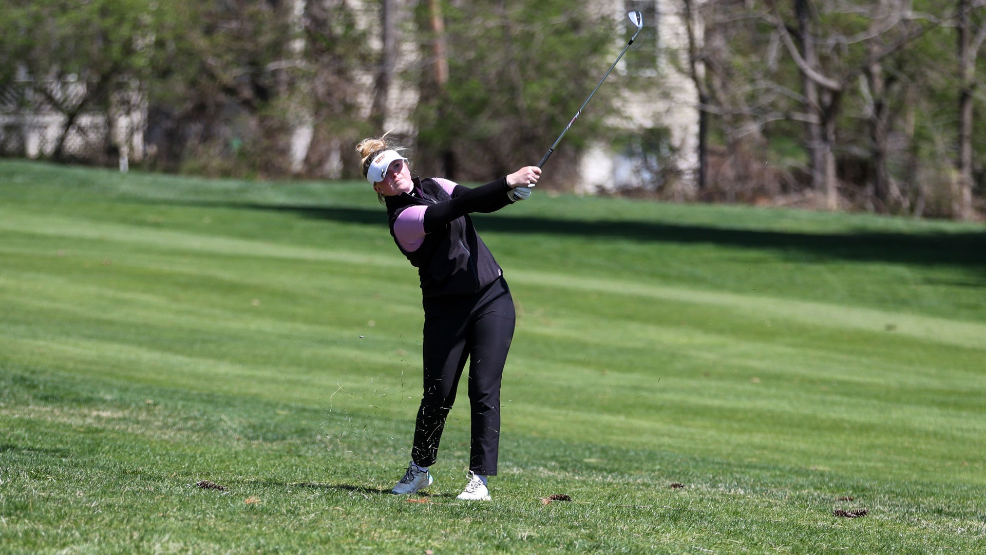 Hanna Lignell wearing black pants, pink polo, and black vest holding follow through after shot from the rough on the first hole at the Cottrell Invitational at Penn Oaks