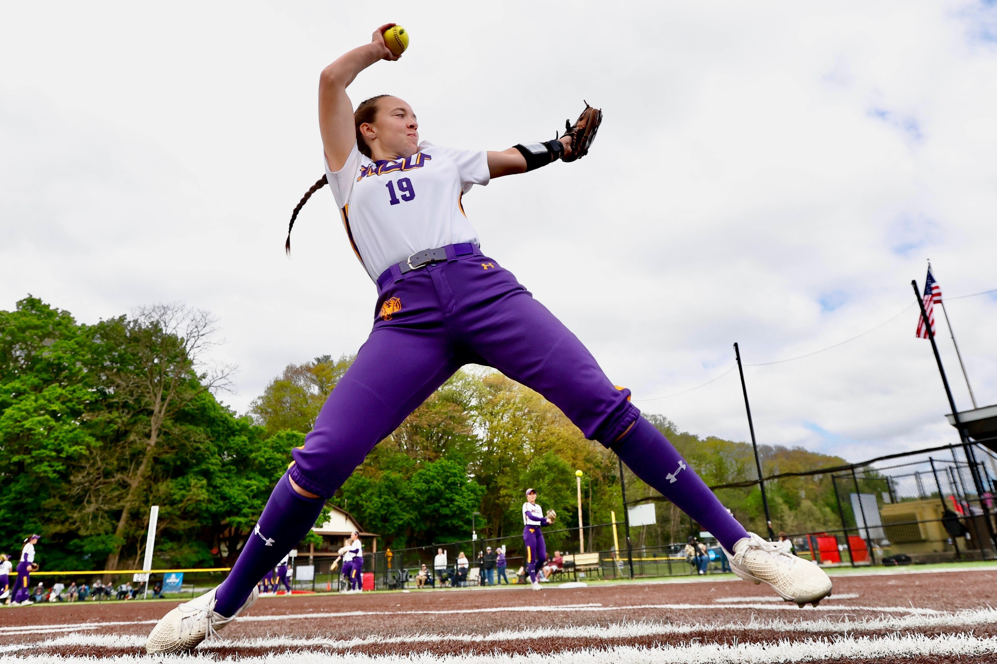 Danielle Ciliberto warms up in-between innings of WCU's NCAA regional against Fairmont State. She is dressed in West Chester's road jerseys with the  white tops and purple-gold stripe down the shoulder and purple pants.