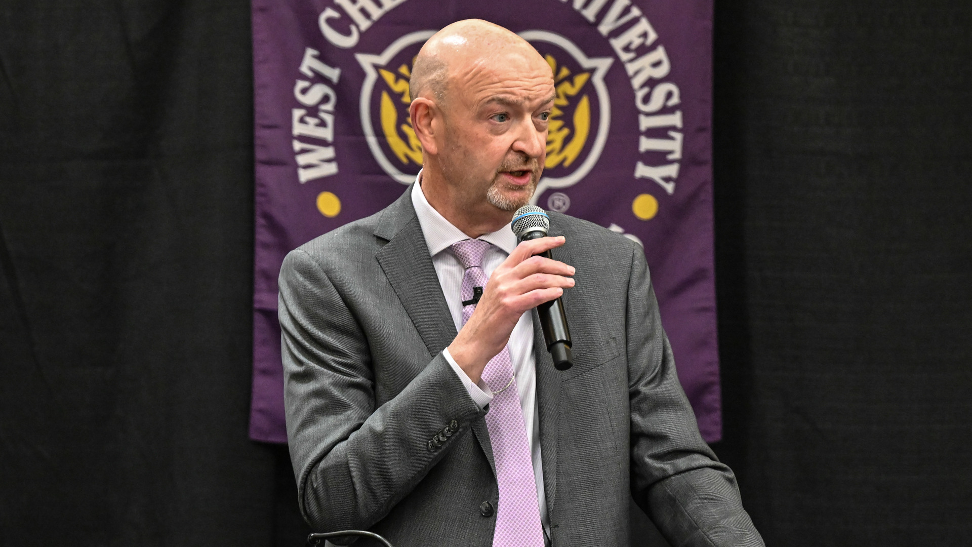 Terry Beattie speaks at the hall of fame banquet in a gray suit with a purple tie