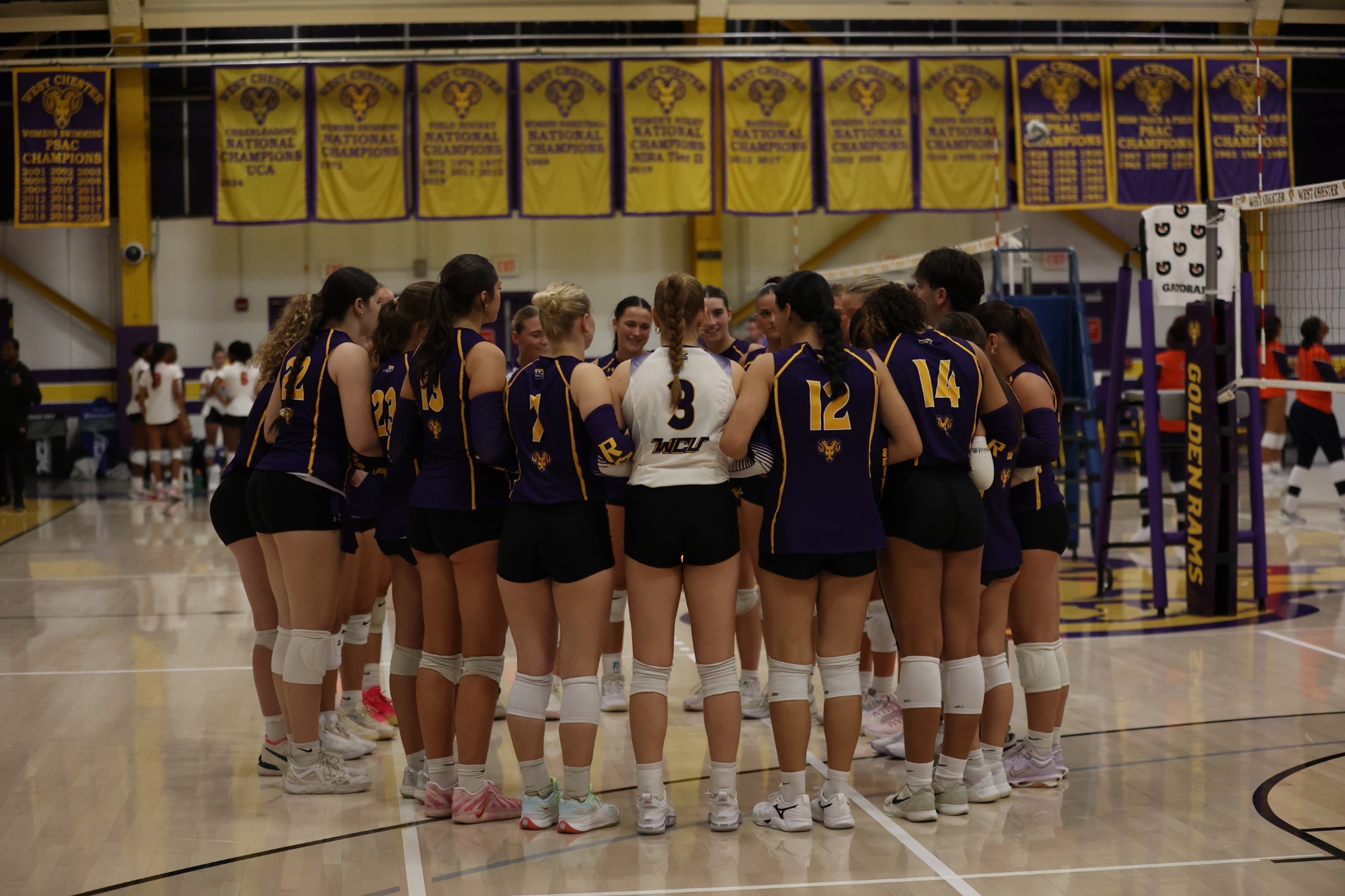 VOLLEYBALL TEAM WEARING PURPLE TOPS WITH LIBERO IN WHITE IN A CIRCLE AT MIDCOURT VS WEST VIRGINIA STATE ON 8-29-26