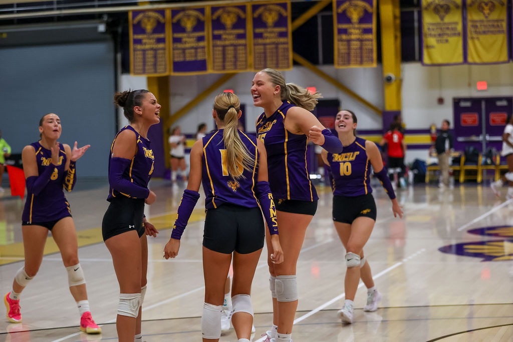 JULIA KWITCHOFF, GWEN ATKINS, AND ADDISON HERTZOG CELEBRATE A POINT AGAINST WVSU ON SATURDAY AFTERNOON IN HOLLINGER FIELD HOUSE. ALL THREE WEARING PURPLE AND GOLD SLEEVELESS JERSEY TOPS