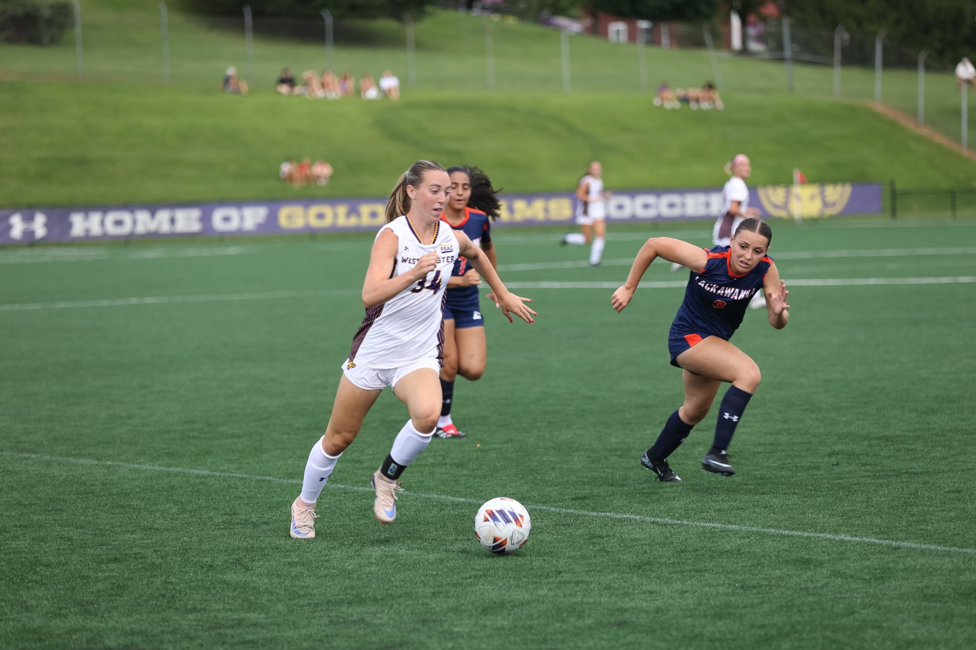 ABIGAIL HANEMANN WEARING HOME WHITE ON WHITE UNIFORM CARRIES THE BALL PAST A PAIR OF LACKAWANNA PLAYERS 