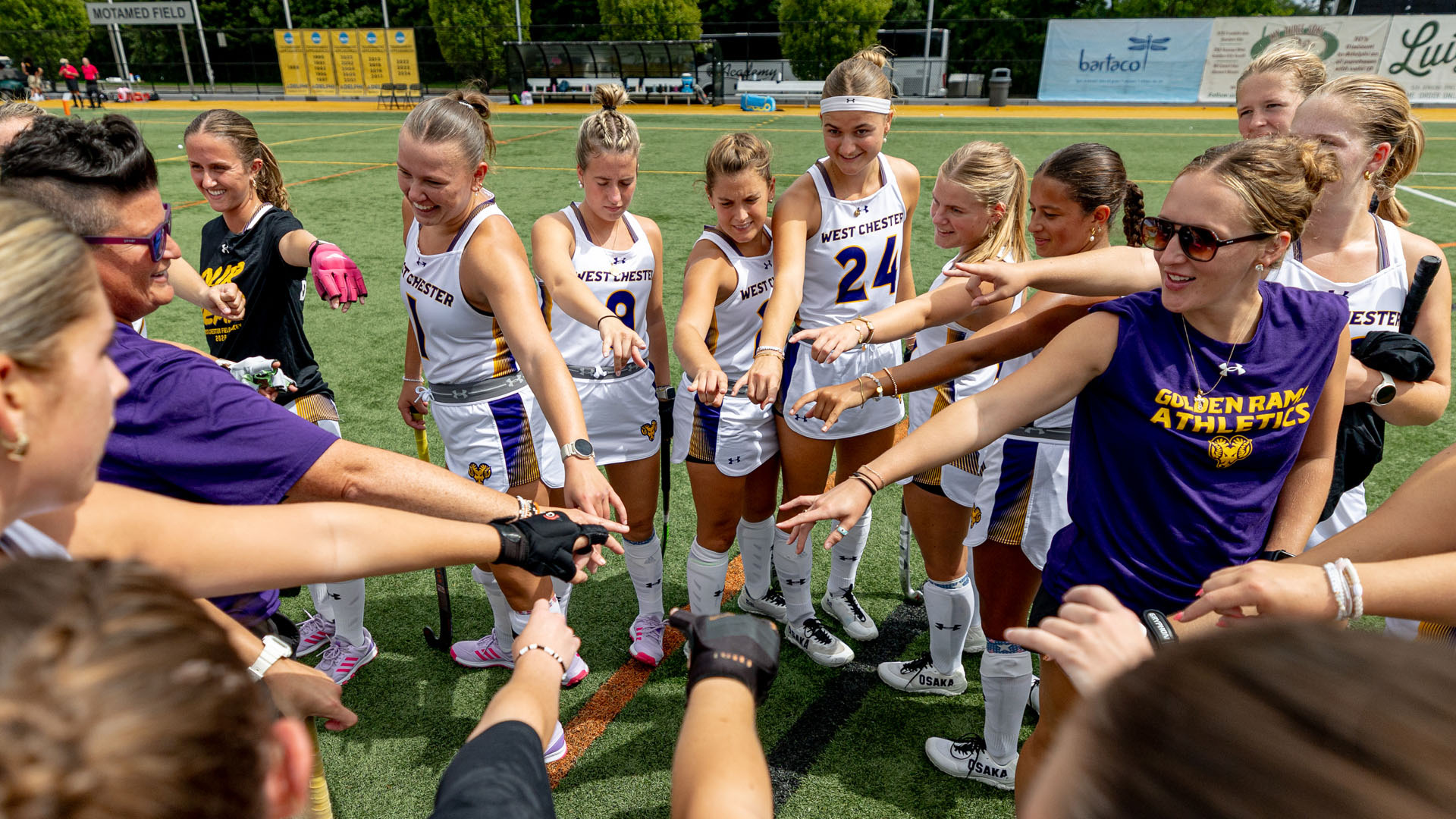 The field hockey team circles up and puts there hands in during pregame talk at Adelphi in their white road uniforms