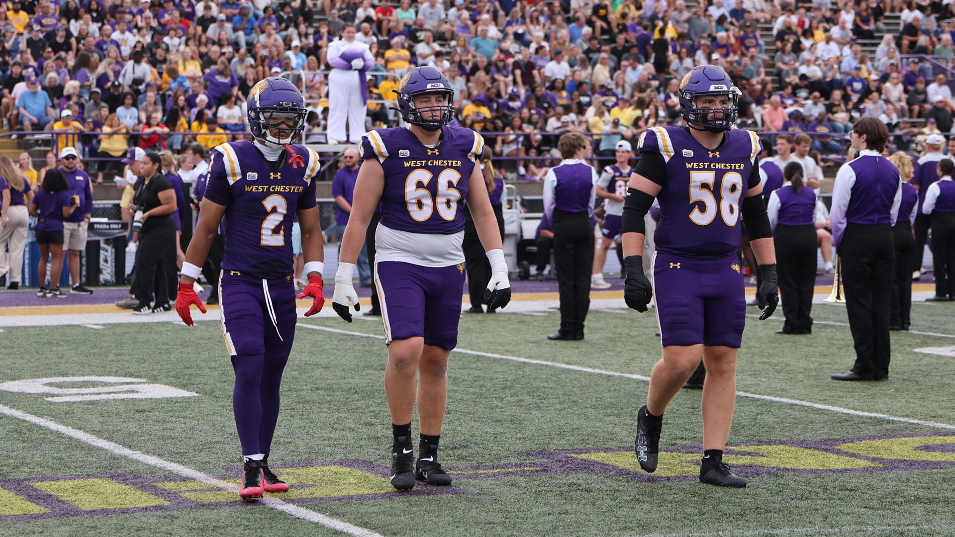 WCU Team Captains (Dylan McKenzie, Cole Kozlowski and Jack Fry) walk to midfield for the opening coin toss dressed in their purple home jerseys with purple helmet and purple pants.