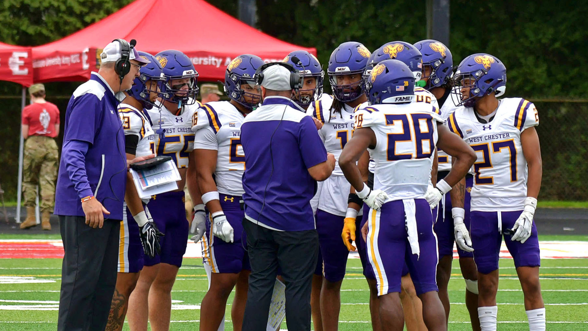 West Chester's special teams unit meets before kickoff on the field with its two coaches wearing their white road jerseys with purple pants at Edinboro.