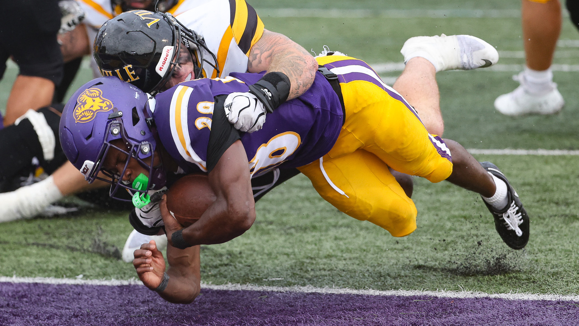 Mick Johnson dives over the goal line for a rushing TD against Millersville at home in West Chester's purple jerseys with yellow pants.