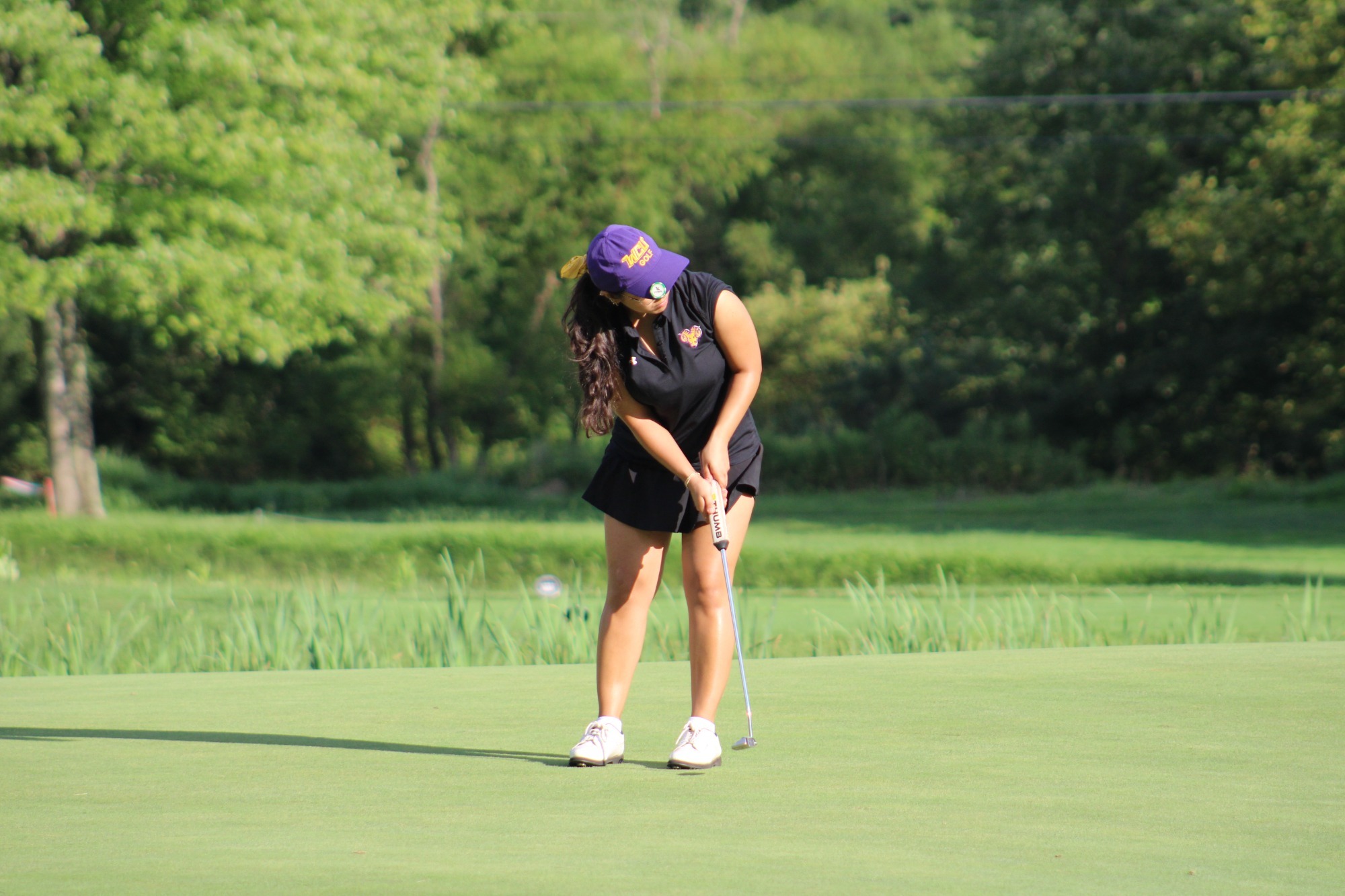 Fatima Rizvi wearing black top and black skirt with purple west chester hat and ball mark attached to hat putting on the green at Penn Oaks
