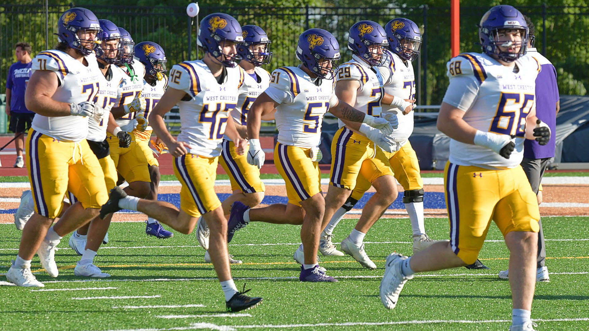Football Team runs out onto the field in their purple helmets, white jerseys and yellow pants before their game at Lincoln.
