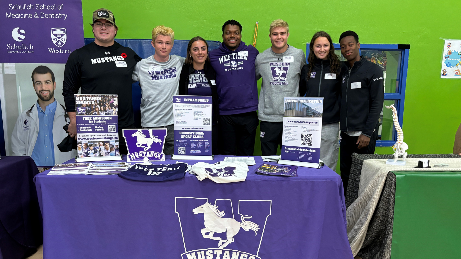 Mustangs at Boys and Girls Club London 2024: Photo of Western University student athletes behind a table at the Boys and Girls Club, with promotional materials about the Western Mustangs on the table