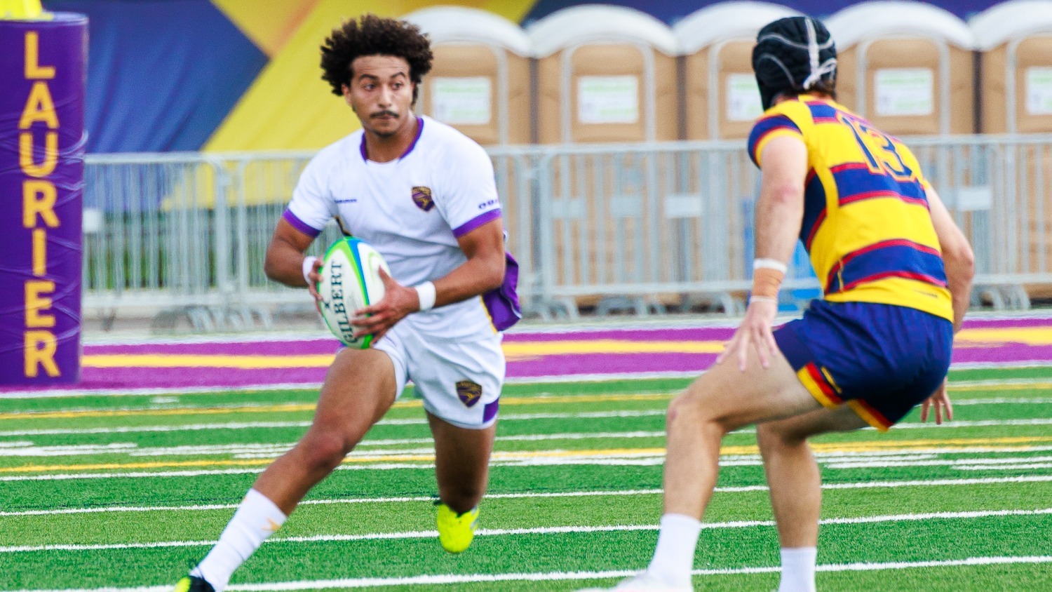 A Laurier rugby player rushes toward a Queen's defender