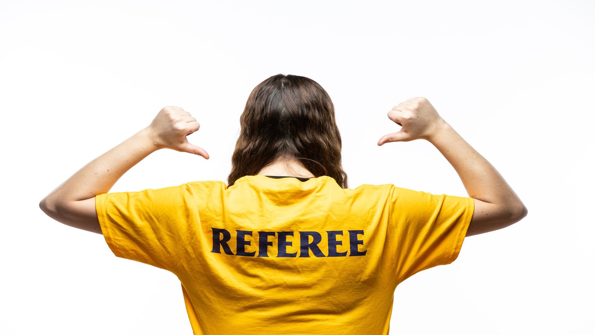 Women's back, wearing yellow t-shirt with REFEREE on the back. Women point to word on her shirt.