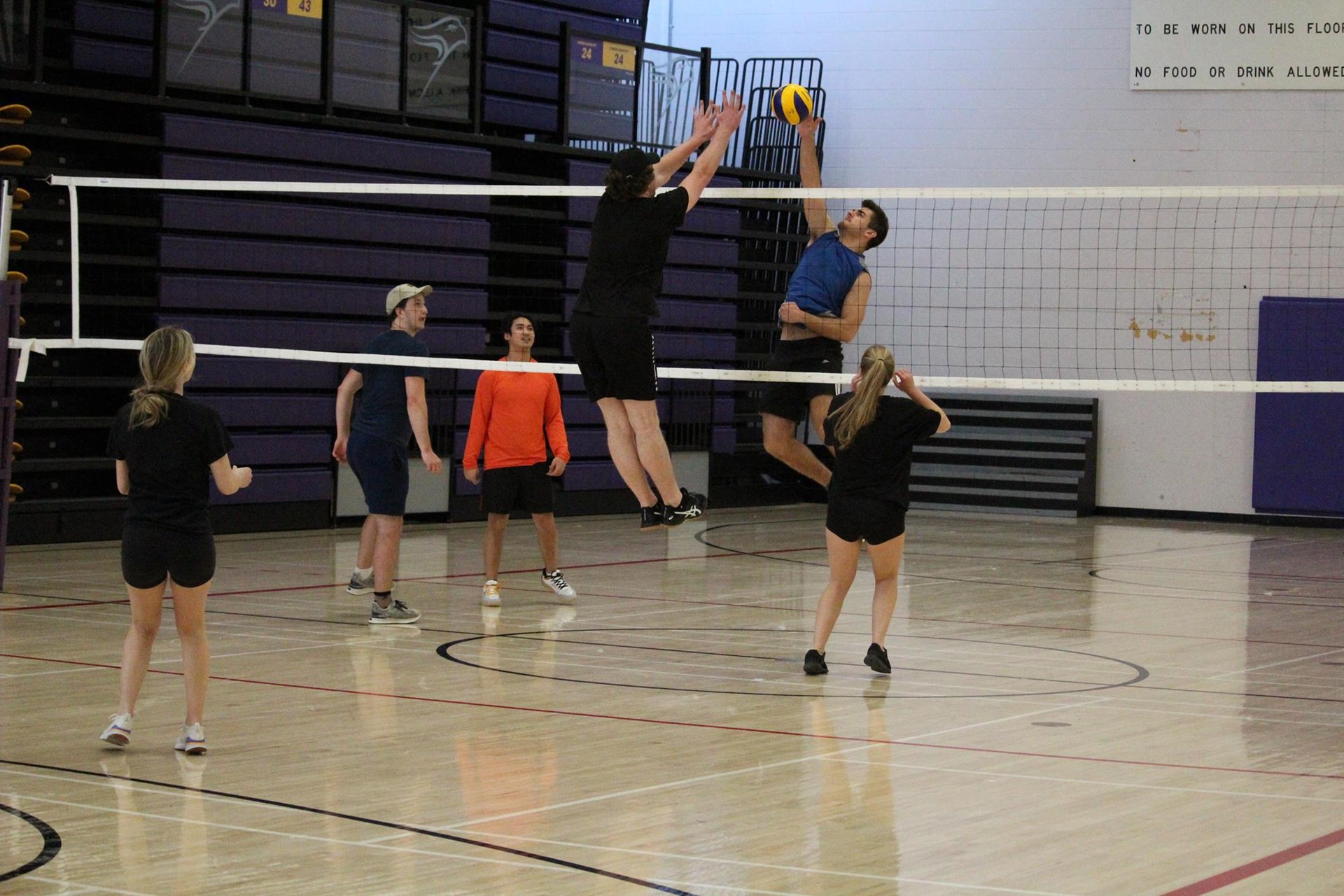 Two volleyball players jousting for a ball at the net with teammates on either side of the net watching