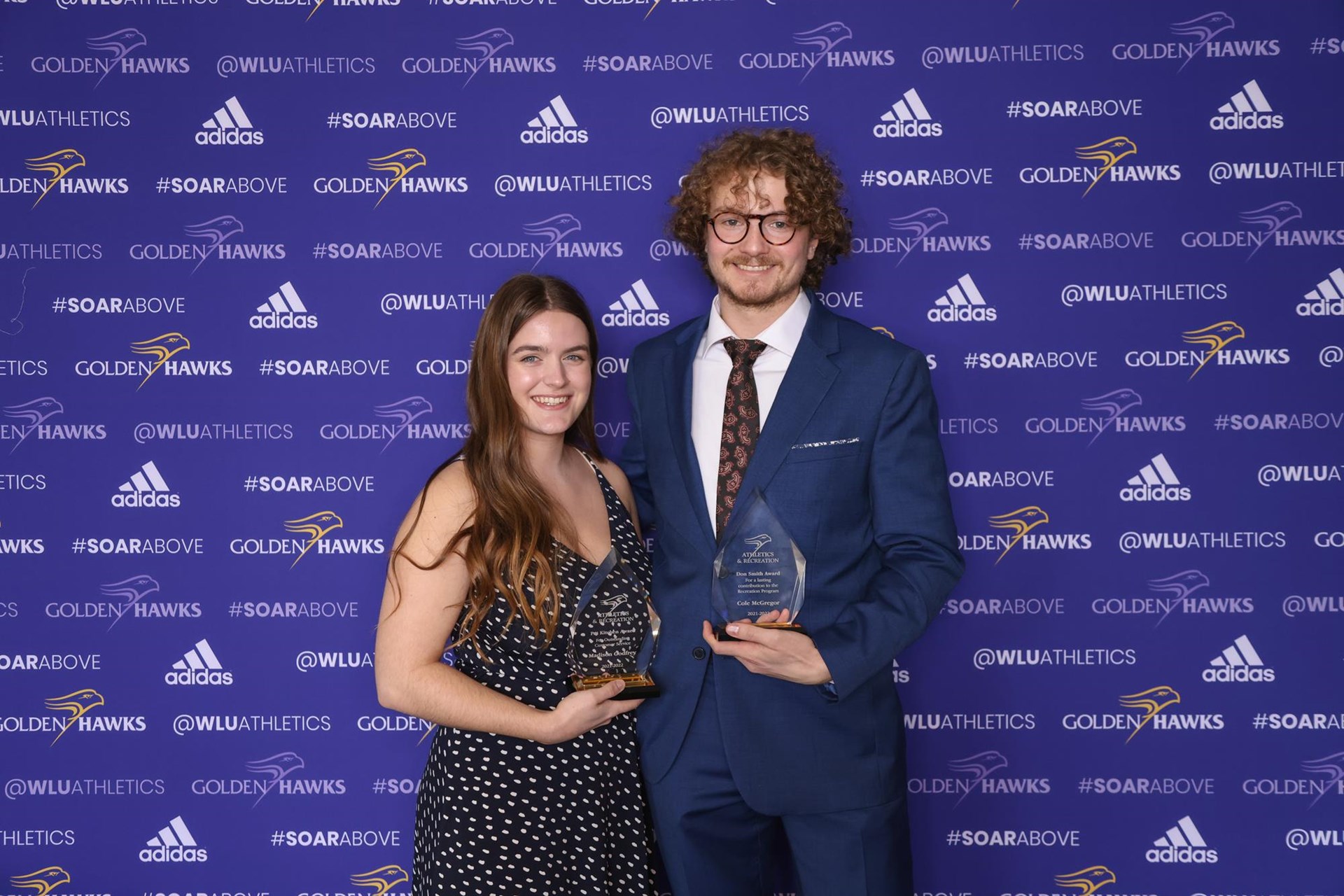 Madison Godfrey (left) and Cole McGregor (right) holding their award trophies in front of Laurier branded back drop