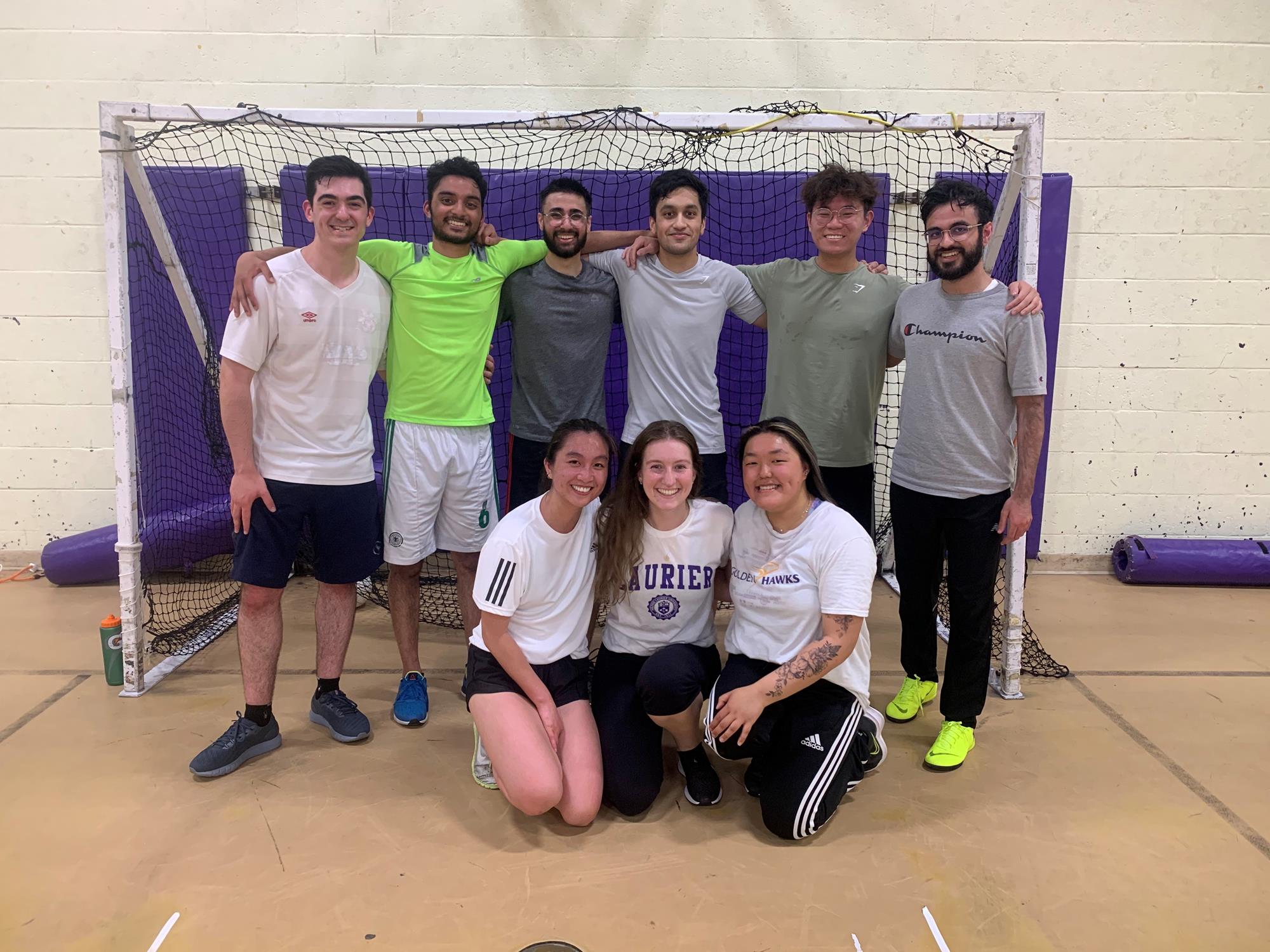 Group of 8 students standing in a group in the stadium gym in front of a soccer net