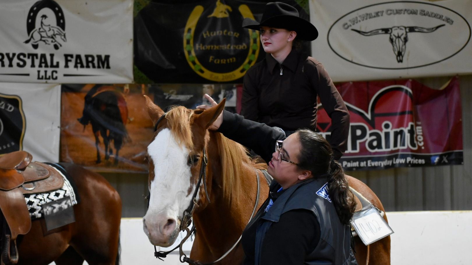 Julie Warnick is on a horse looking to her right while coach McKenna Debus handles the horse
