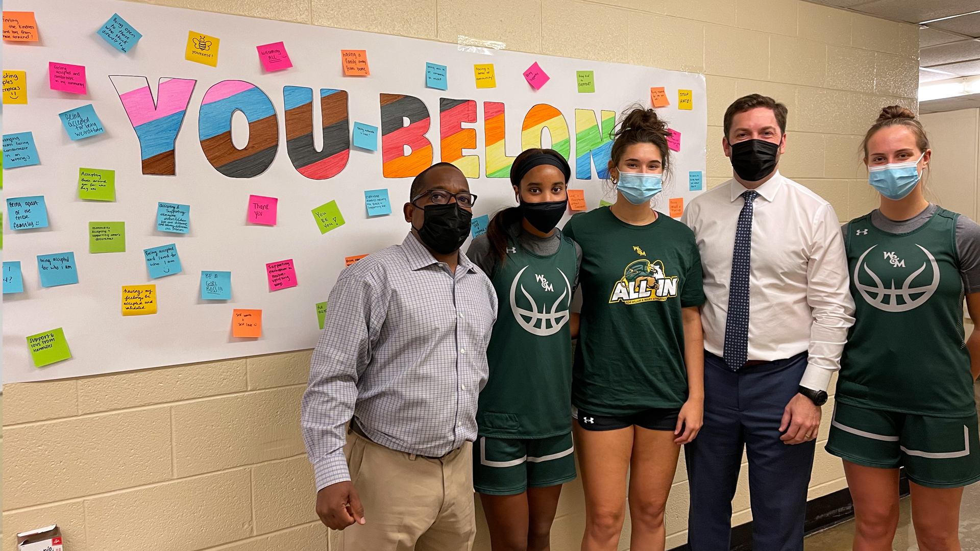 AD Brian Mann, Jason Simms and student-athletes stand in front of the You Belong board in Kaplan Arena.