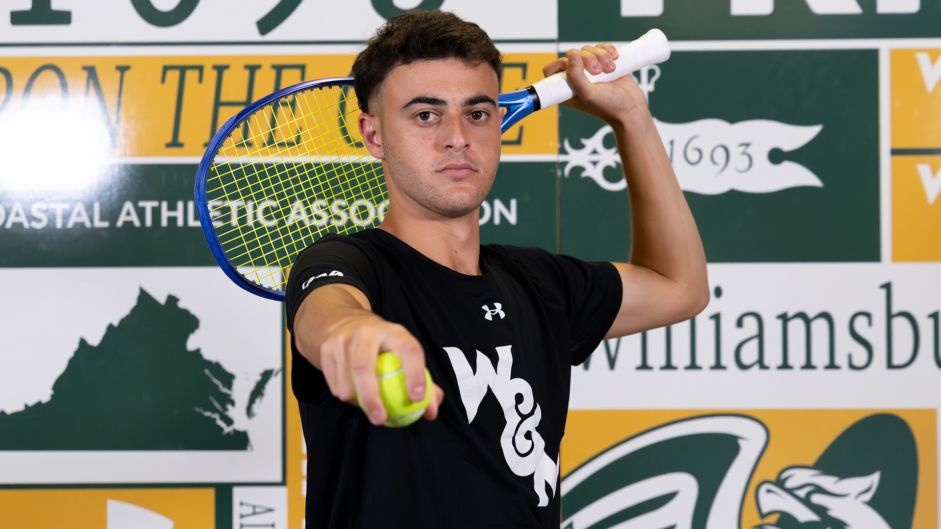 Gur Trakhtenberg holds a ball in front and his raquet behind his head against the scrapebook backdrop on media day. 