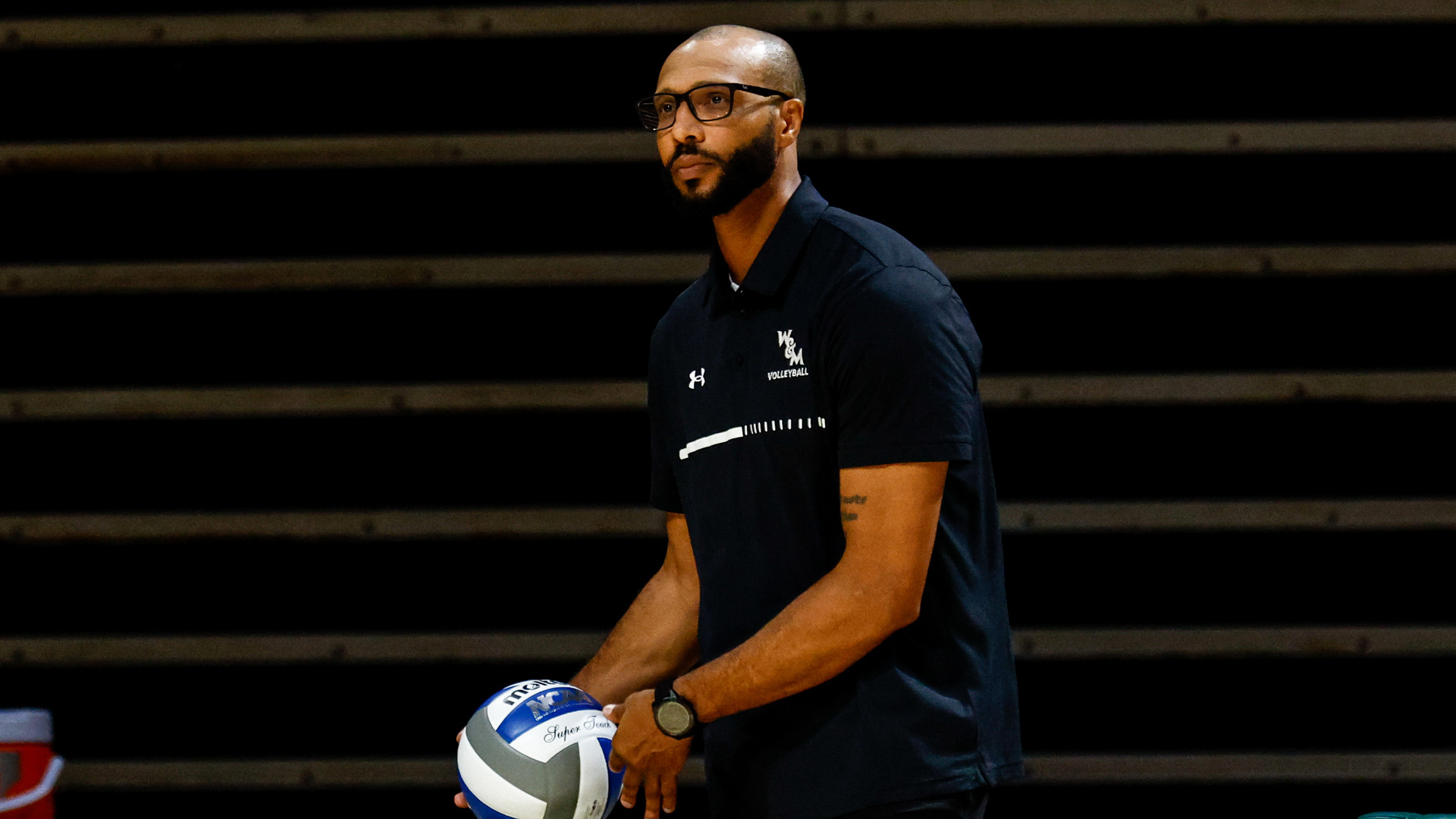Ryan Adams holds a volleyball as he looks toward the court at Kaplan Arena