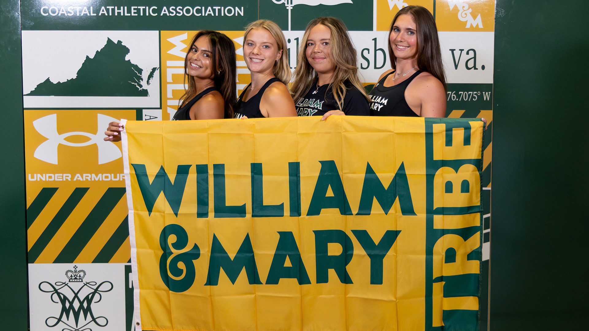 Sia Chaurdy, Francesca Davis, Yaelle Vaissaud, and Parker Debnam hold a William & Mary Tribe flag in front of the scrapbook backdrop on media day. 
