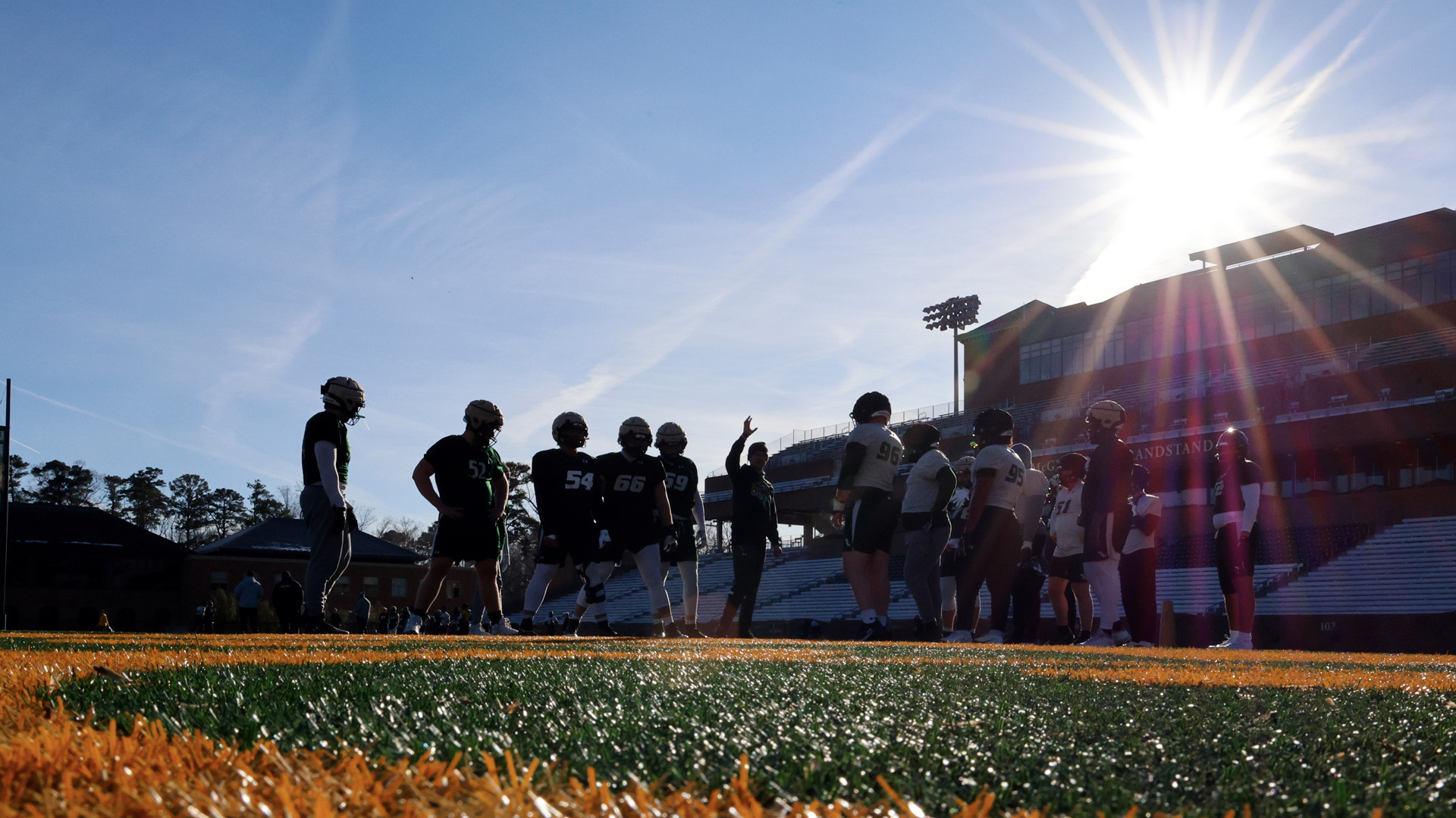 Members of the W&M football team stand on the field at Zable Stadium as the sun sets behind the grandstands