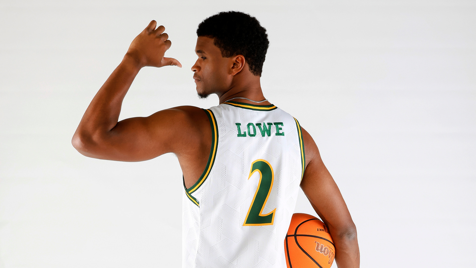 Chase Lowe stands with his back to the camera and points at his last name on the back of his jersey with his thumb. 