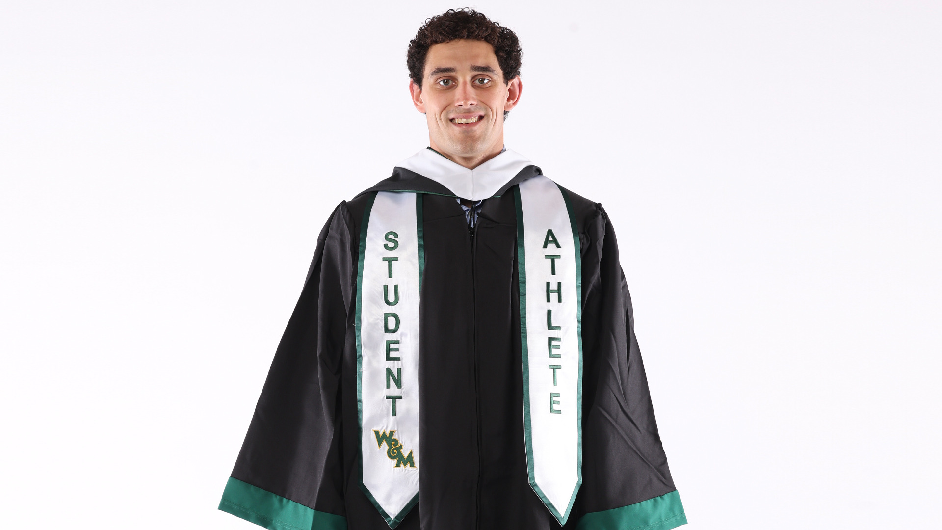 Will Glass stands and smiles during a graduation photo shoot with his gown and white student--athlete stole. Glass competed in swimmming for four years and earned his degree in government and history. 