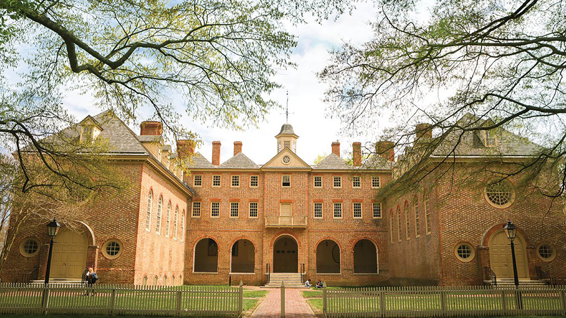 The view of the Wren Building looking from the Sunken Gardens during the fall with no trees on the leaves and students walking by. 