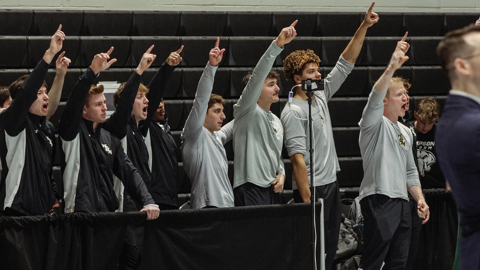 Members of the William & Mary men's gymnastics team stand in a line with their hands raised in the air during the ECAC Championship meet.