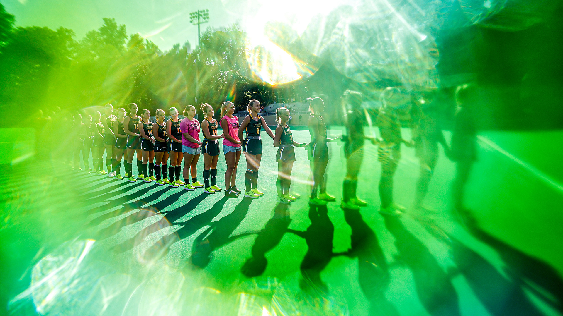 Tribe field hockey stands hand and hand for the national anthem prior to its match vs. American in 2025. The photo has a green gel over it to add an artsy feel.