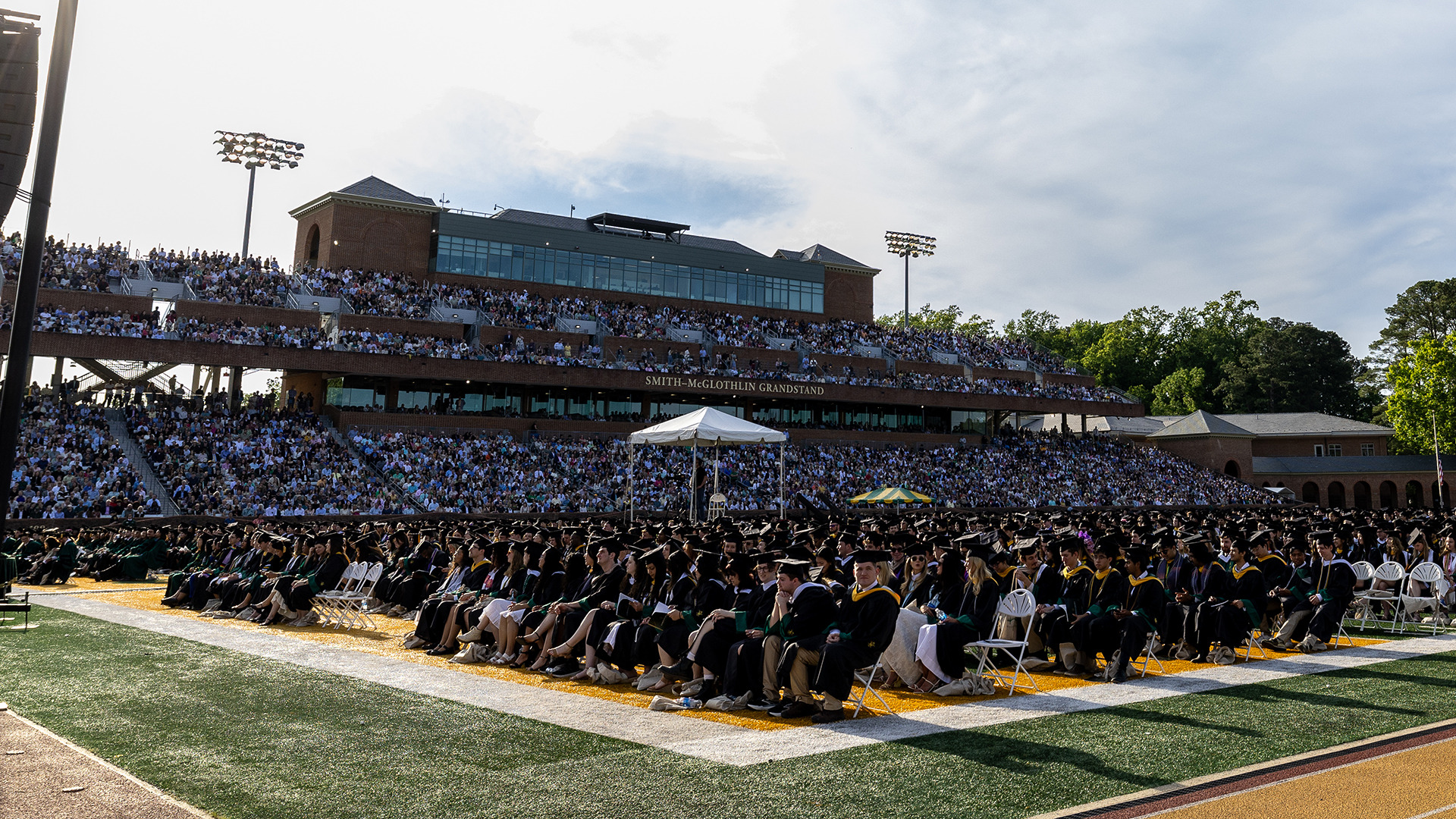 William & Mary Commencement with graduating students in chairs on the Zable Stadium turf and the view of a full McGloughlin Grandstand with parents and friends. 