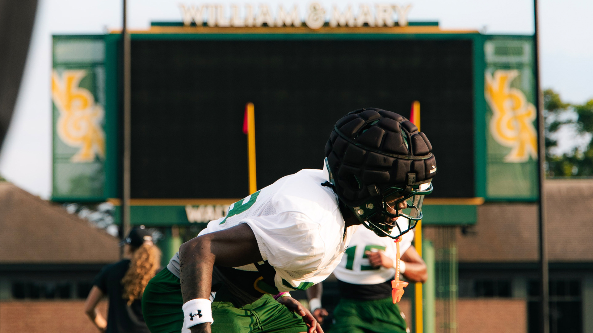 W&M Football Player stretches on the field at Zable Stadium with the video board in the background