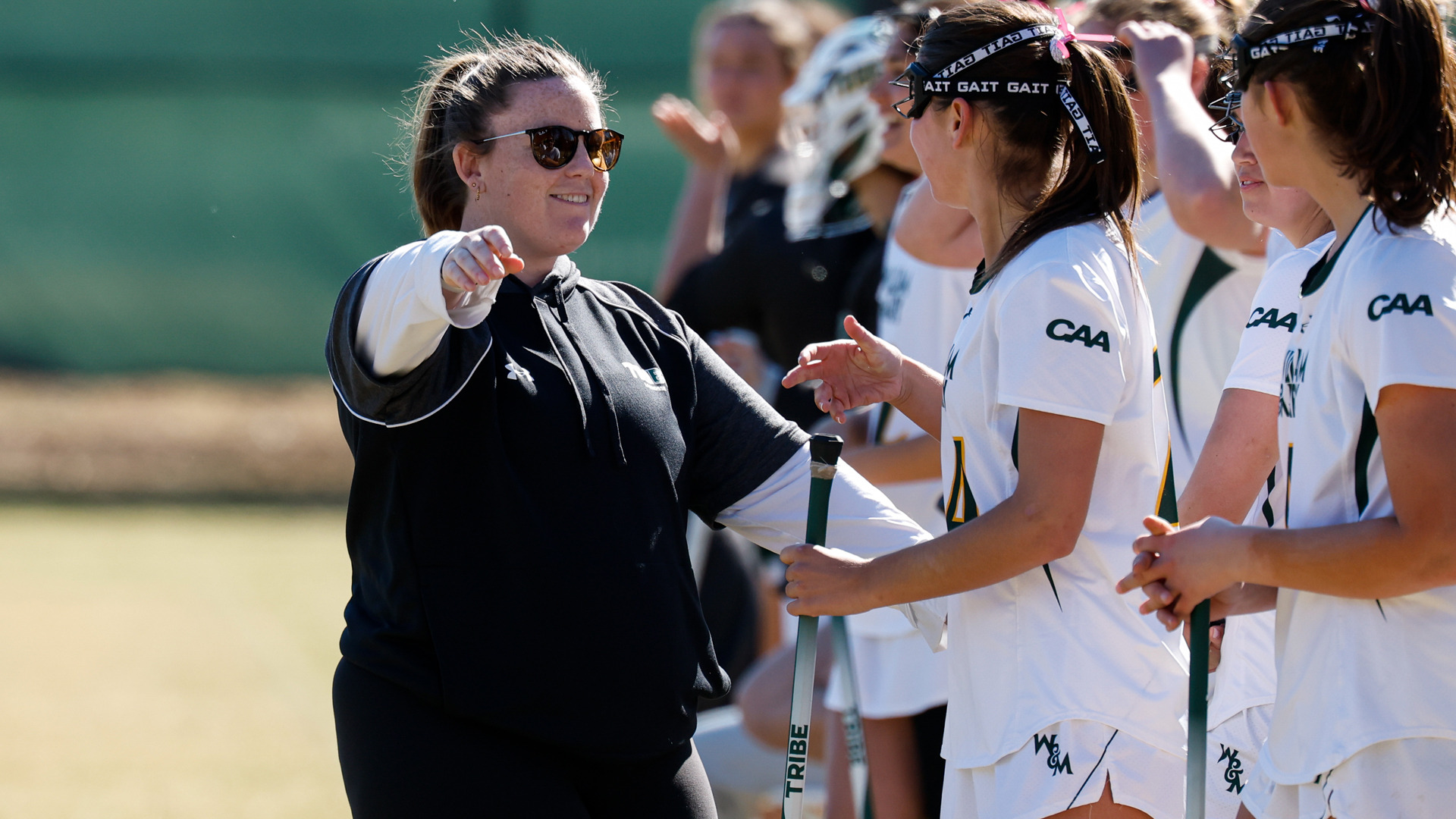 Katie Lasater smiles as she points towards the field while coaching players during a game.